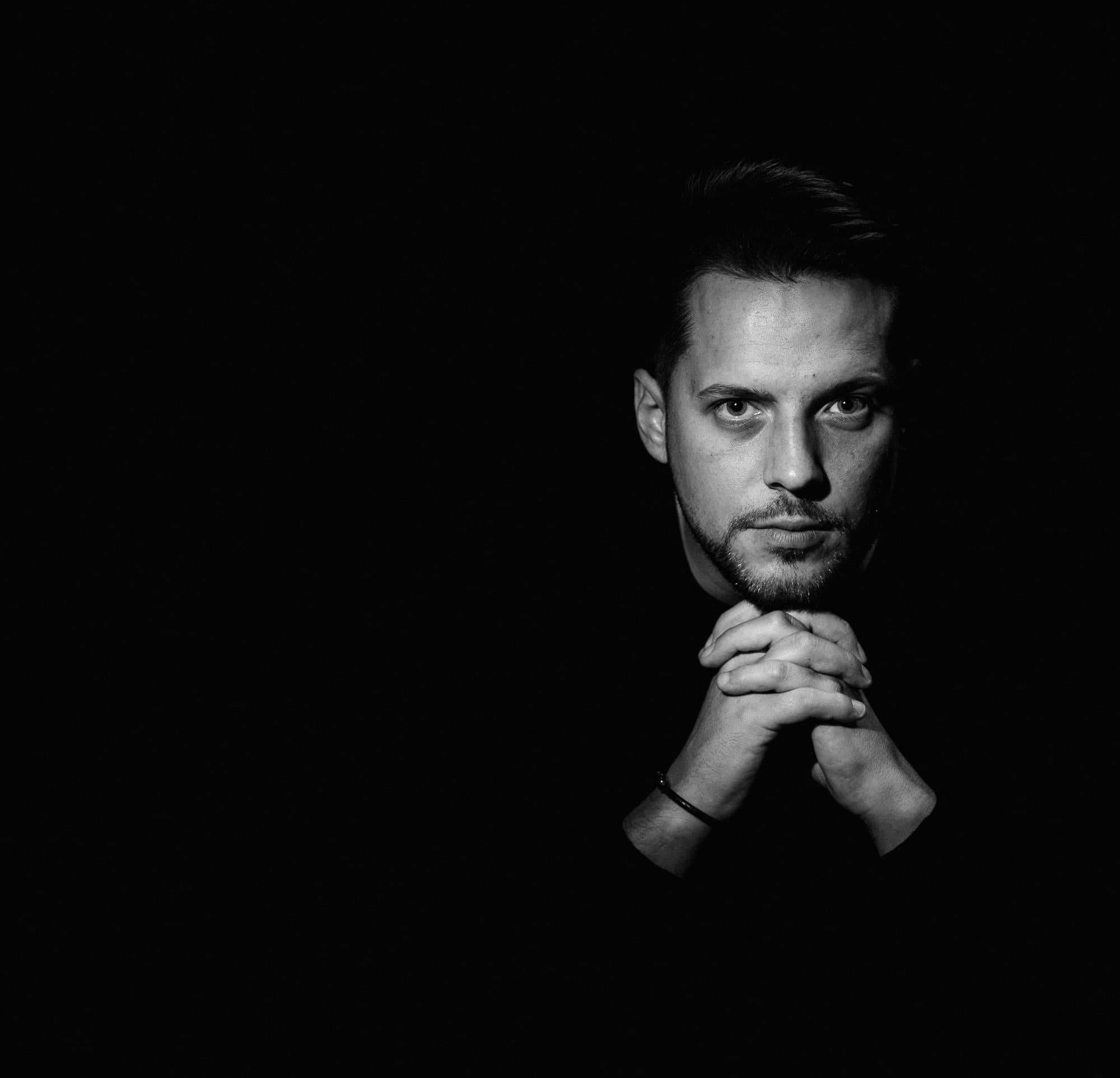 low-key studio portrait in palma, man with hands clasped, dark background