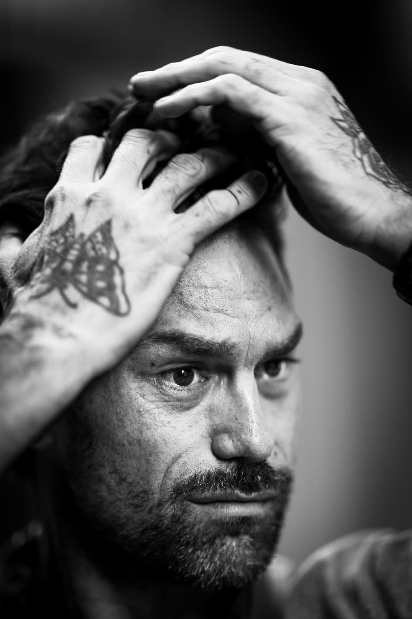 editorial studio portrait in palma, man with tattoos, hands in hair, strong expression
